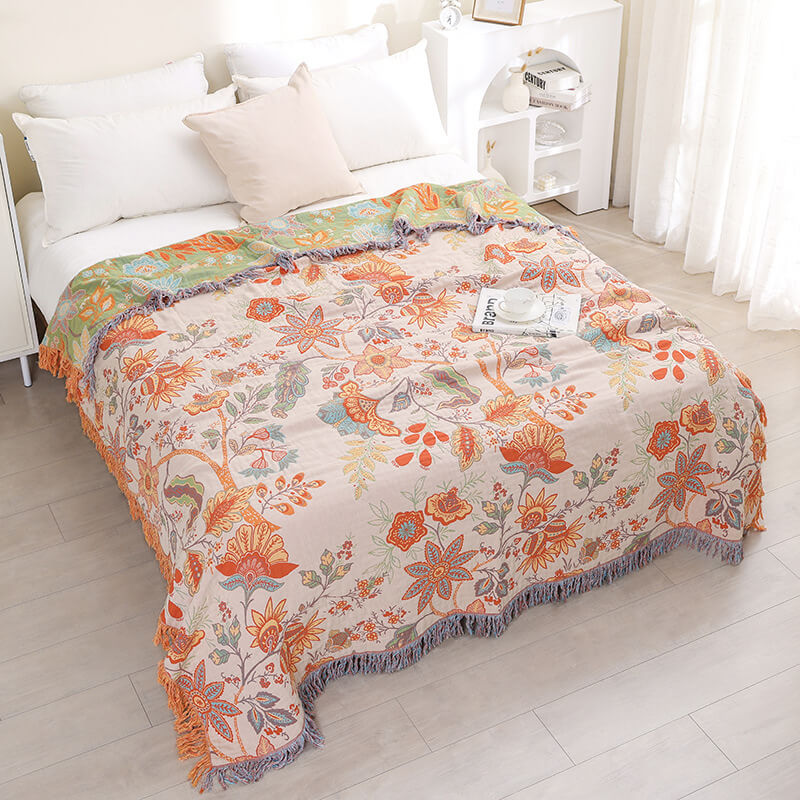 Boho floral jacquard throw blanket with orange and blue botanical patterns spread across a white bed in a bright modern bedroom.