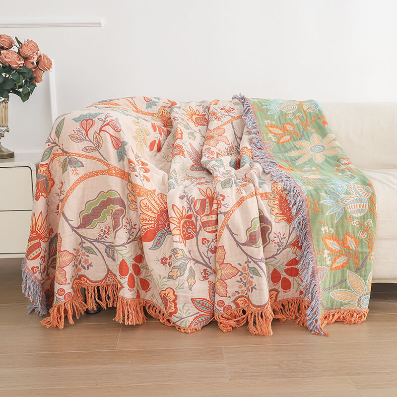 Reversible boho floral jacquard throw blanket styled on a sofa, showing both the beige and sage green sides with decorative fringe.