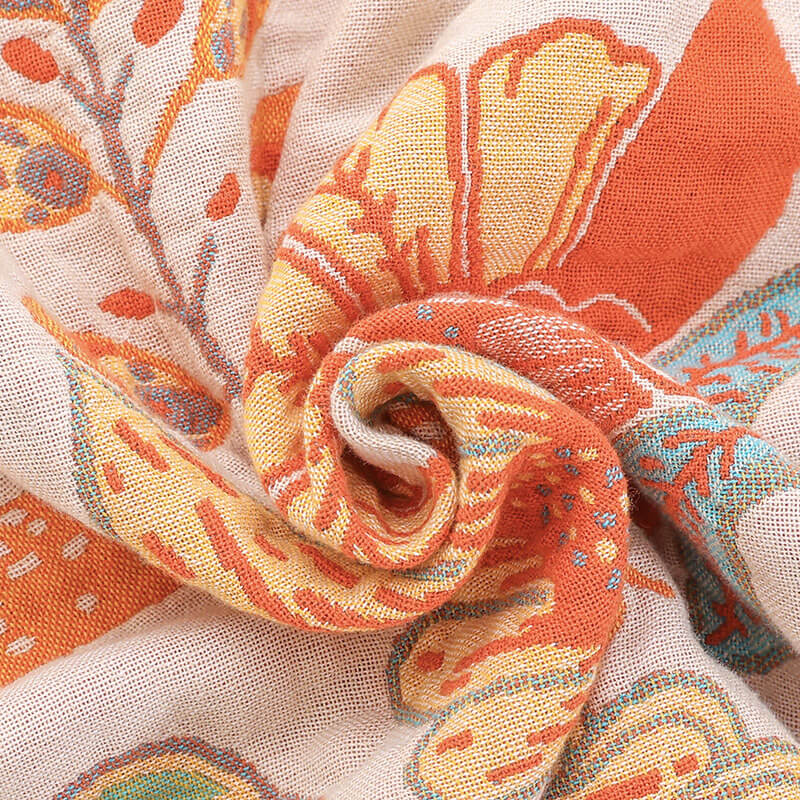 Detailed macro shot of the breathable jacquard fabric texture of a boho floral blanket featuring orange, yellow, and teal woven threads.