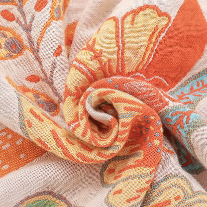 Detailed macro shot of the breathable jacquard fabric texture of a boho floral blanket featuring orange, yellow, and teal woven threads.