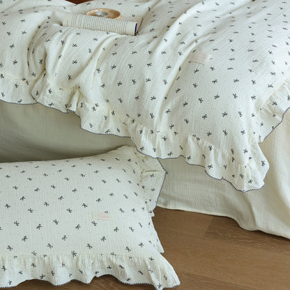 Detail image showing the ruffled pillowcase and muslin duvet cover with small bow prints. Focuses on the soft, cream-colored fabric.