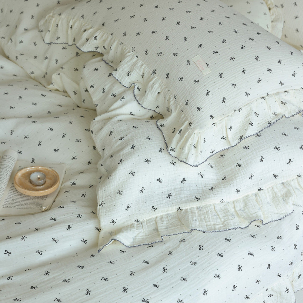 Overhead shot of the double gauze bedding showing the ruffled pillow shams and the delicate black bow pattern against the white cotton.