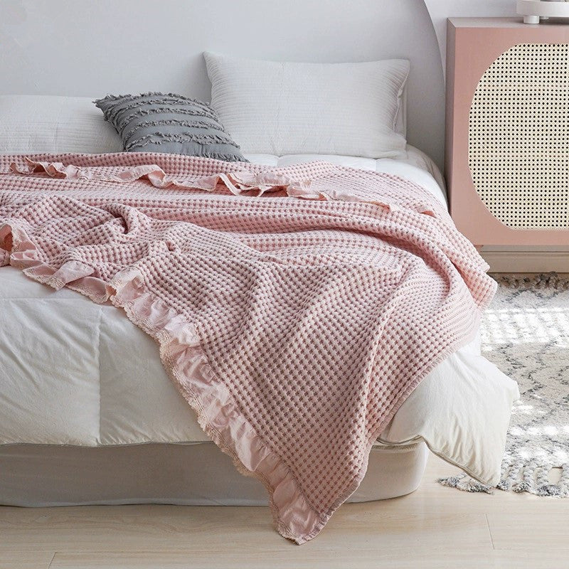 Soft pink waffle throw blanket with lace edge details on a cozy duvet.