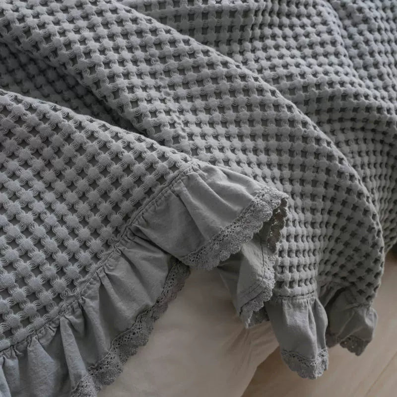 Close-up of grey cotton waffle blanket showing breathable woven texture and lace ruffle edge.