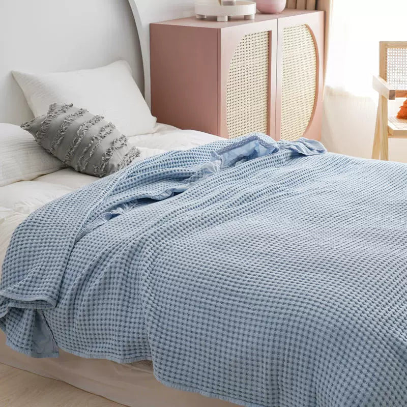 Soft blue breathable waffle throw blanket draped over bed linens in a bright room.