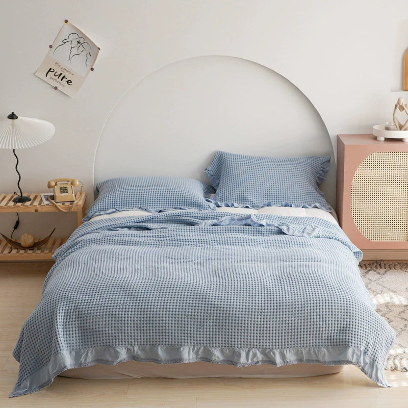 Light blue cotton waffle blanket and pillow shams with elegant ruffle trim on a bed.