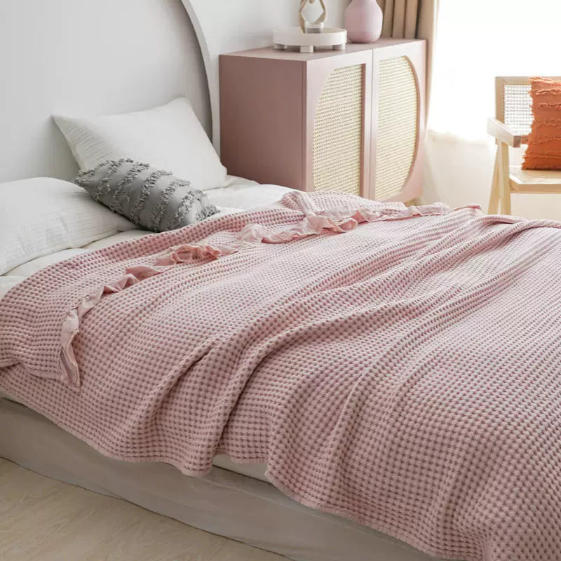 Lightweight pink cotton waffle blanket with elegant ruffle border in a bright bedroom.