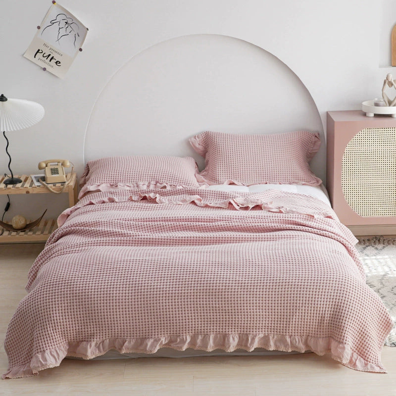 Full view of a pink breathable cotton waffle blanket with ruffles on a white bed.