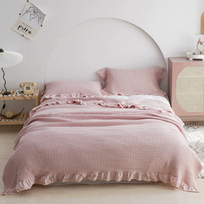 Full view of a pink breathable cotton waffle blanket with ruffles on a white bed.