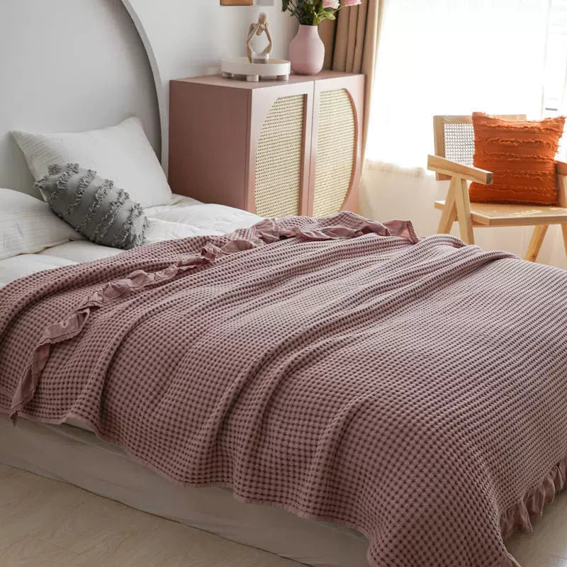 Soft and cozy dusty rose waffle weave throw blanket draped over a bed.