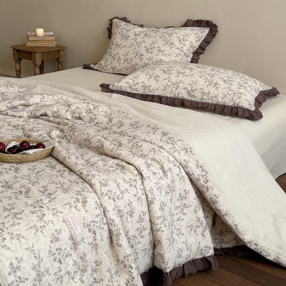 Brown floral cotton comforter draped across an ivory bed with matching ruffled pillows