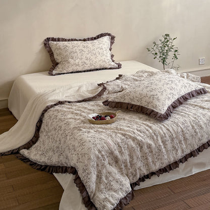 Full bed scene with brown floral comforter, mocha ruffled lace trim, and ivory bedding