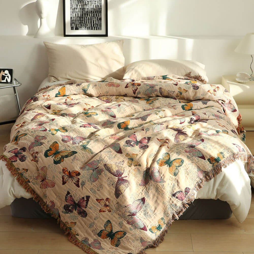 Butterfly cotton throw blanket with fringe styled on a cream bed