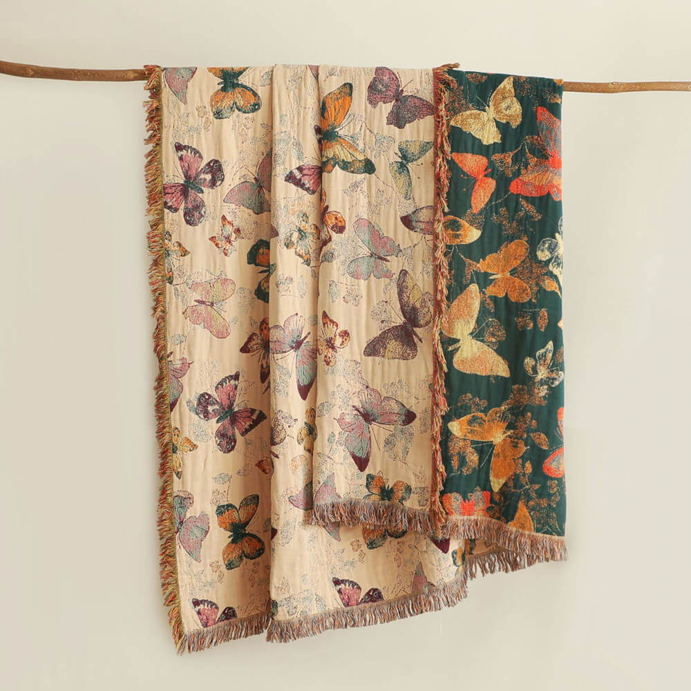 Butterfly cotton throw blanket hanging on a wooden rod showing beige side and deep teal reverse