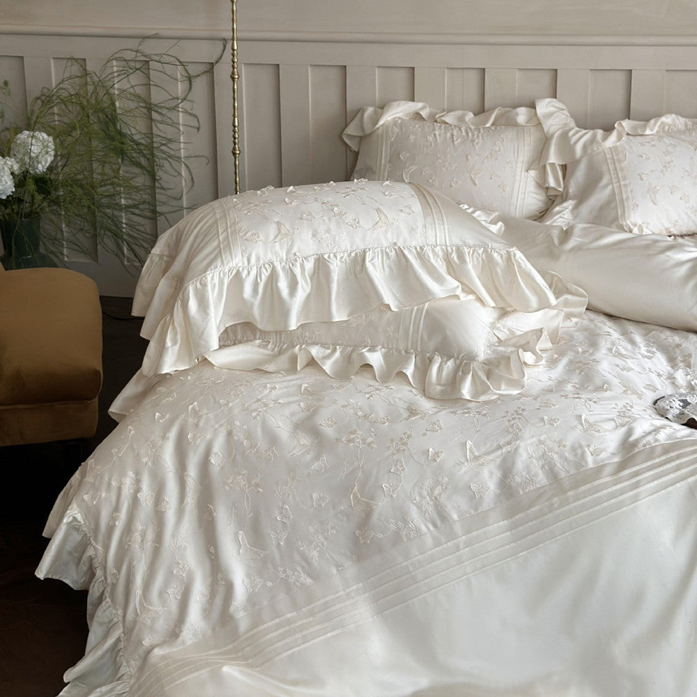 White embroidered bedding set on a bed with a neutral-colored headboard.