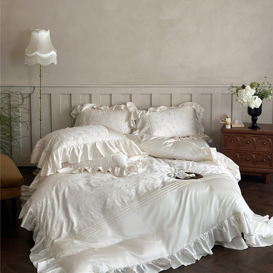 White ruffled bedding set on a bed in a bedroom with a lamp and dresser.