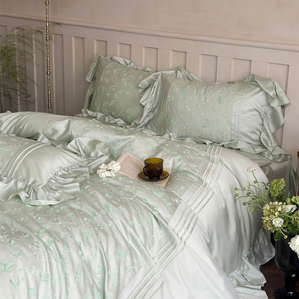 Overhead view of the light green Butterfly Embroidered Bedding Set featuring ruffles and a book on the duvet.