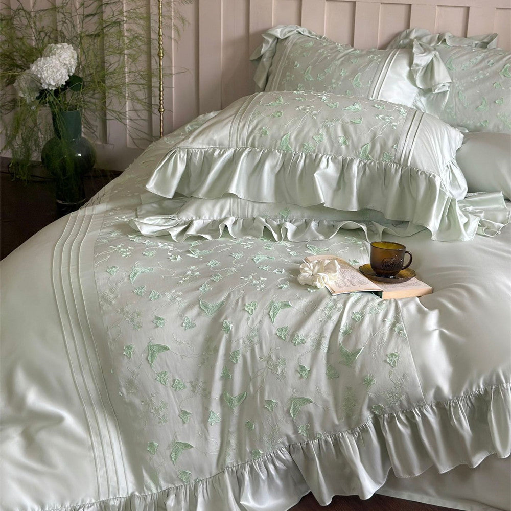 Close-up of light green bedding showing butterfly embroidery detail, ruffles, and pintucks.