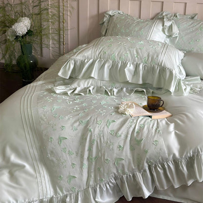 Close-up of light green bedding showing butterfly embroidery detail, ruffles, and pintucks.