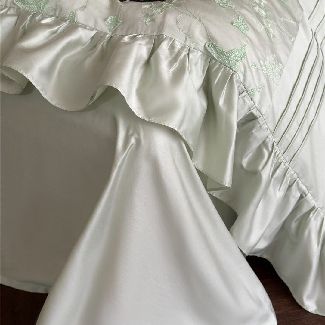 Detail of the silky ruffled edge and butterfly embroidery on the light green duvet cover.