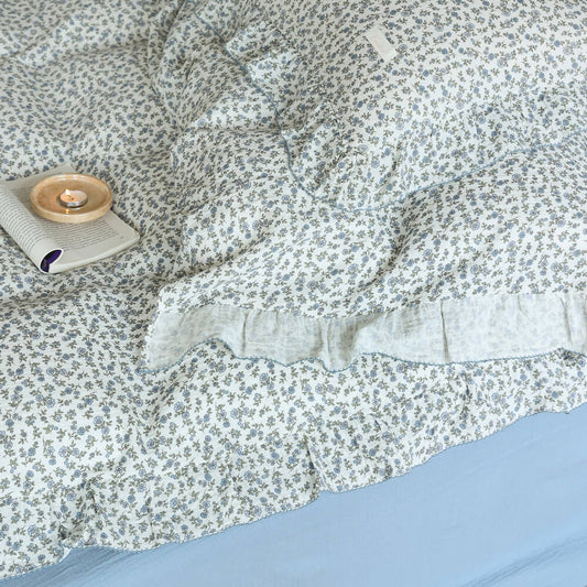 Floral-patterned comforter on a bed with a candle and small pillow.