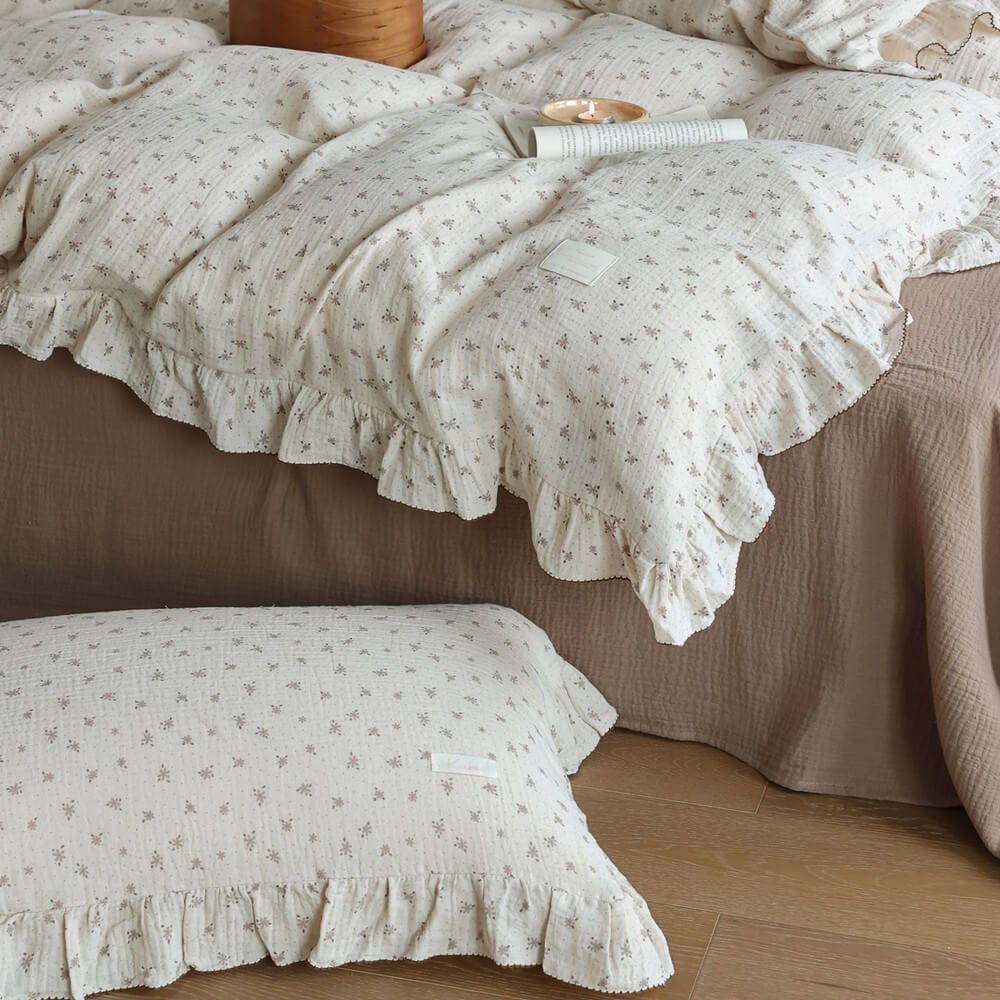 Detailed shot of the ruffled edge of the floral muslin duvet cover and a matching pillow on the floor, emphasizing the soft, airy cotton gauze fabric.