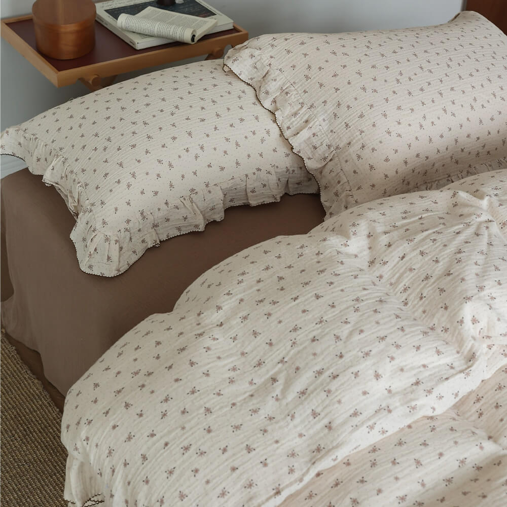 Overhead view of two ruffled floral muslin pillow shams and the cotton gauze duvet cover, highlighting the delicate small flower pattern and crinkled texture.