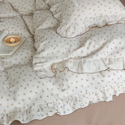 Top-down view of the floral muslin duvet cover and pillow sham, clearly showing the ruffle trim, the light brown floral print, and a small lit candle on the bed.
