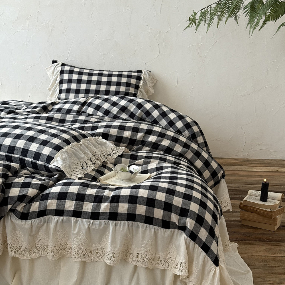 Black and white checkered duvet with lace trim on a bed in a room with a textured wall and plants.