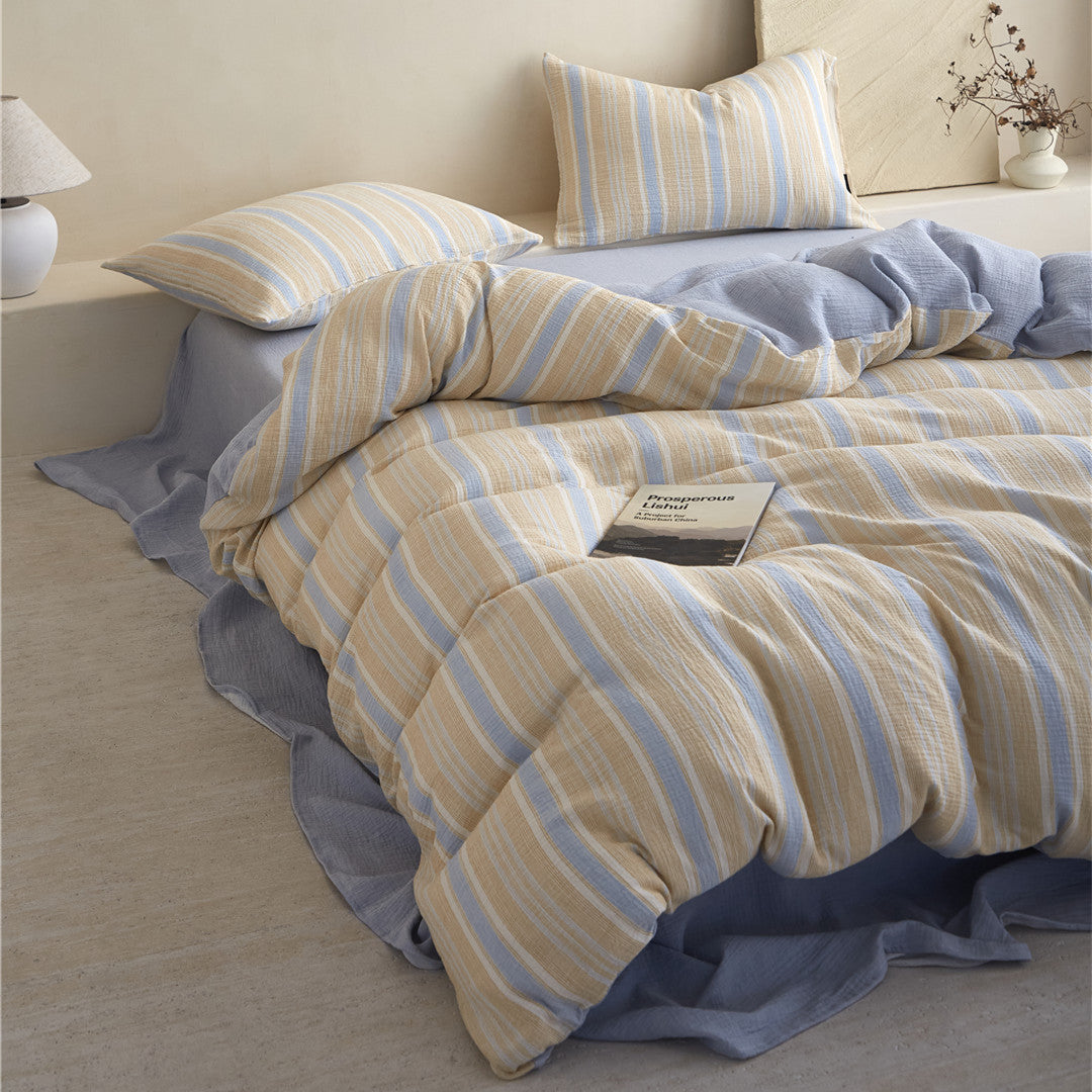 Mid-shot of the Yellow & Blue Striped Reversible Bedding Set, styled with striped pillow shams in a bright, minimalist room.