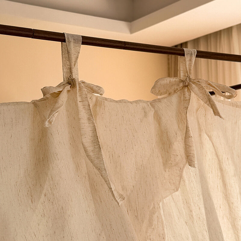Beige curtains with tied ribbons hanging from a rod against a neutral wall.