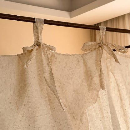 Beige curtains with tied ribbons hanging from a rod against a neutral wall.