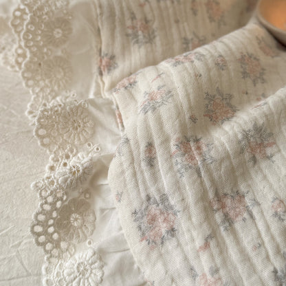 Macro photography of the high-quality woven linen-cotton blend fabric on a quilted floral throw blanket with intricate lace borders.