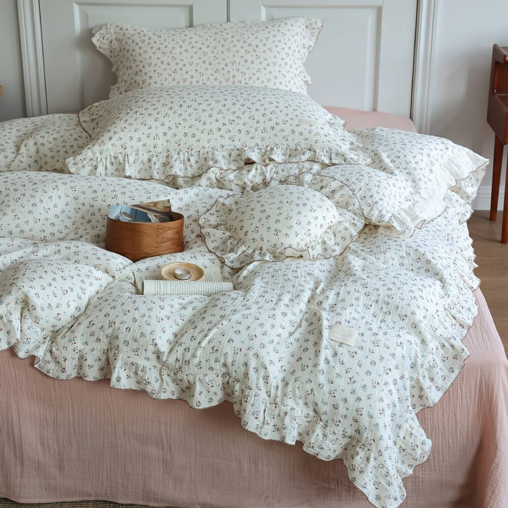 Full view of a bed dressed with a complete 'Baby's Breath' print cotton muslin duvet cover set, including multiple pillows and a decorative wooden box, against a white headboard.