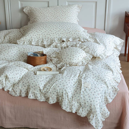 Full view of a bed dressed with a complete 'Baby's Breath' print cotton muslin duvet cover set, including multiple pillows and a decorative wooden box, against a white headboard.