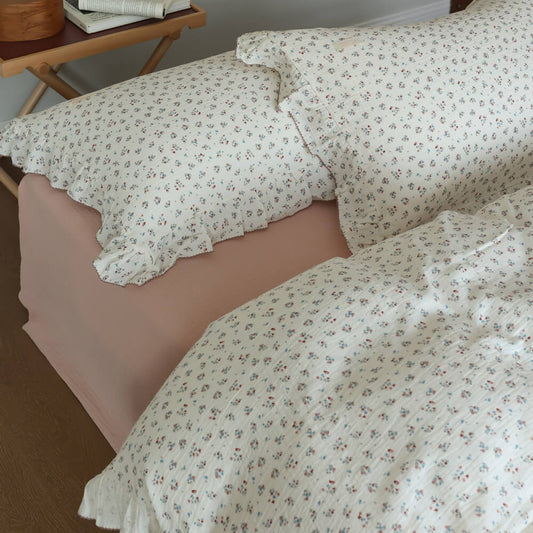 Cotton muslin duvet cover set with tiny blue and red floral 'Baby's Breath' print and ruffled edge, shown on a bed with a soft pink fitted sheet.