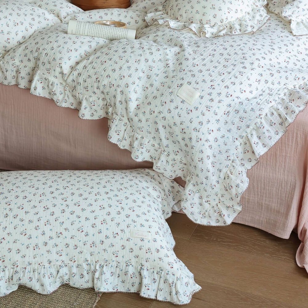 Front view of cotton muslin duvet cover and multiple pillows with delicate 'Baby's Breath' pattern and ruffled trim, accented with a subtle brown stitching.