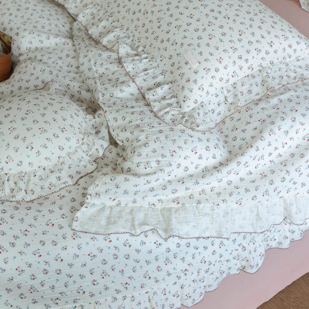 Close-up of cotton muslin duvet cover and pillowcase featuring 'Baby's Breath' floral print and elegant ruffles, with a pink bed skirt visible.