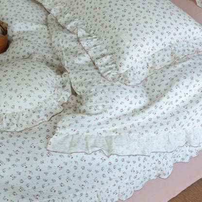 Close-up of cotton muslin duvet cover and pillowcase featuring 'Baby's Breath' floral print and elegant ruffles, with a pink bed skirt visible.