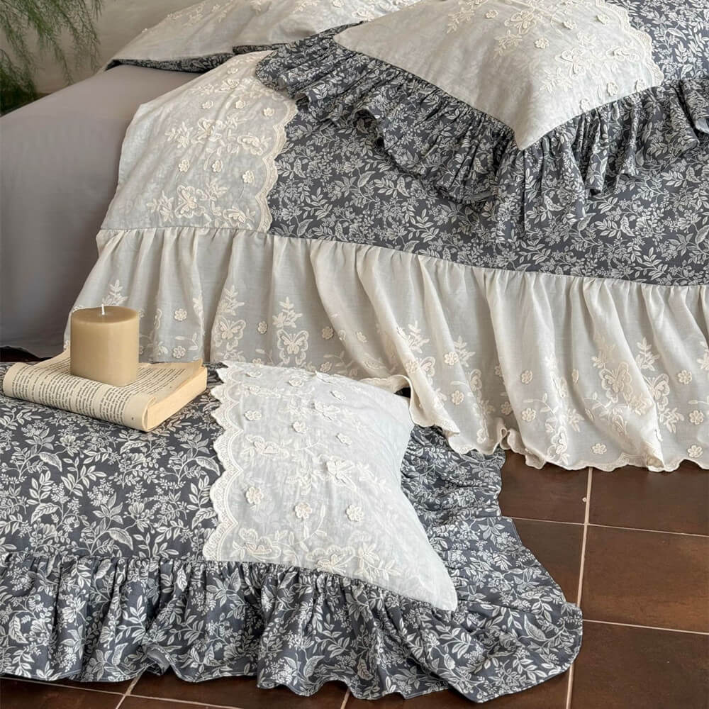 Detail of gray floral ruffled bedding with ivory embroidered panels and small cushion