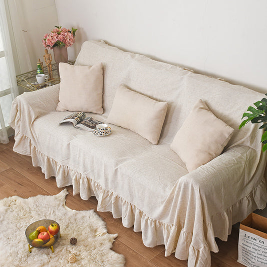A cozy beige ruffled sofa cover, draped over a light-colored sofa with a magazine and throw pillows, creating a natural and warm living room atmosphere.