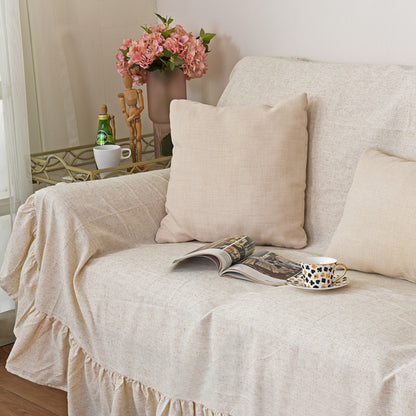 A close-up shot of the natural style beige sofa cover, highlighting the textured fabric and ruffles, with a throw pillow, a magazine, and a teacup on the couch.