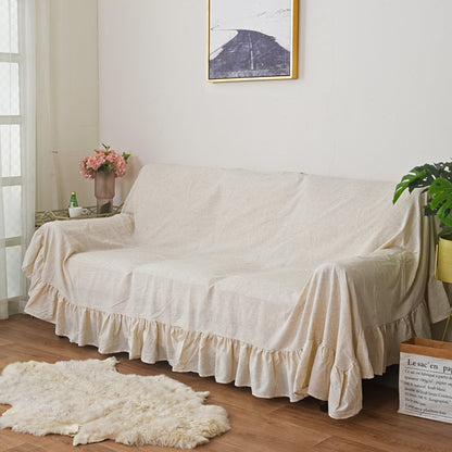 The beige ruffled sofa cover on a couch in a living room, with a soft rug on the floor and a large piece of wall art, providing a clear view of the entire slipcover.