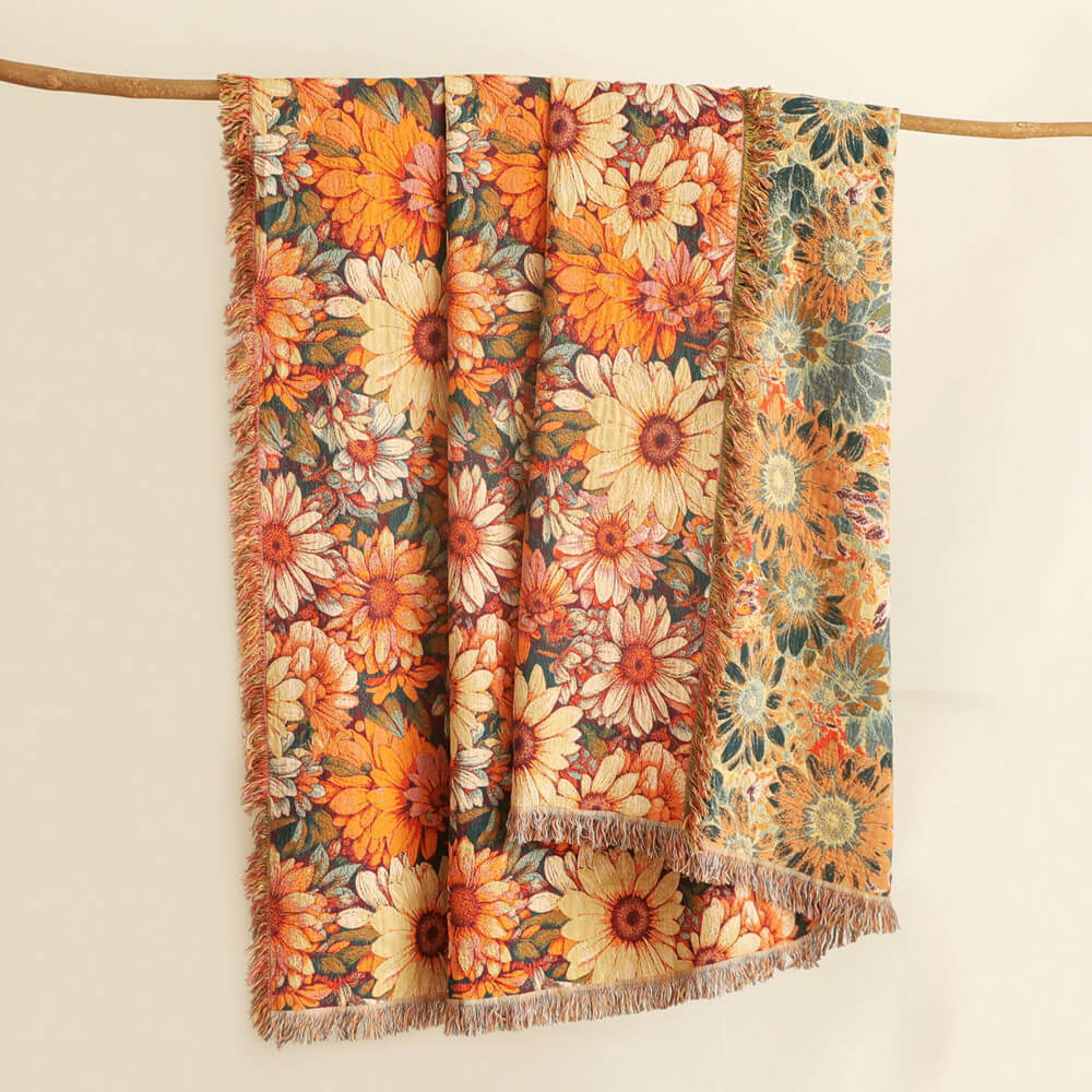 Daisy floral cotton throw blanket hanging on a wooden rod, showing warm orange florals, reverse side, and fringe edges
