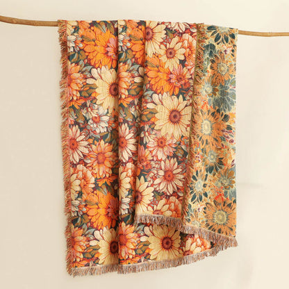 Daisy floral cotton throw blanket hanging on a wooden rod, showing warm orange florals, reverse side, and fringe edges