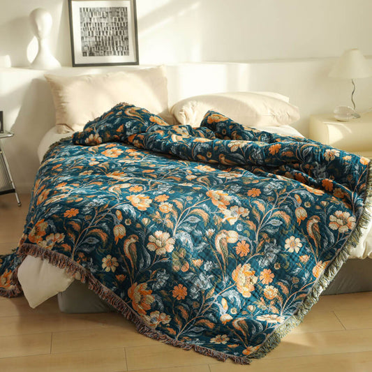 Dark teal botanical cotton throw blanket with fringe layered across a bed