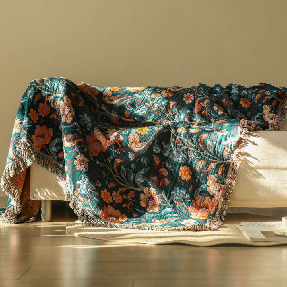 Dark teal botanical cotton throw blanket draped over a cream sofa