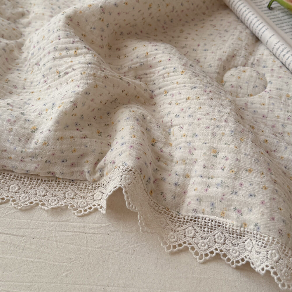Detailed macro shot of soft, breathable crinkled cotton gauze fabric with a pastel ditsy floral print and exquisite embroidered lace trim edge.