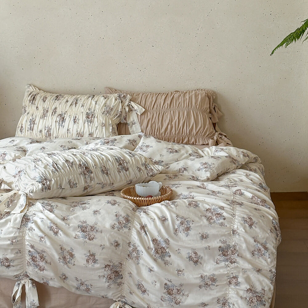 Faded rose floral bedding set in a neutral cottage bedroom with ruched pillows, cotton muslin fabric, and soft beige tones.