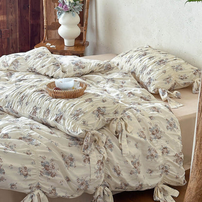 Close-up of faded rose floral bedding with cotton muslin fabric, ruched duvet design, ribbon ties, and soft beige bedroom styling.